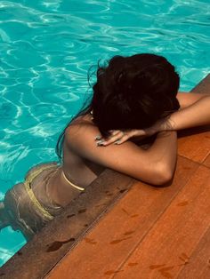 a woman sitting on the edge of a swimming pool next to a wooden dock with her hands behind her head