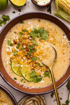 a bowl of soup with limes, corn and cilantro on the side