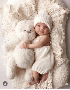 a baby is laying next to a white teddy bear