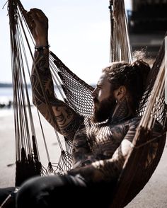 a man with tattoos sitting in a hammock