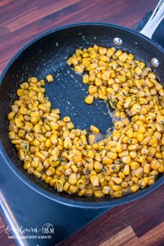 corn frying in a skillet on top of a wooden table with tongs