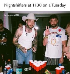 two men standing next to each other at a table with cups and drinks on it