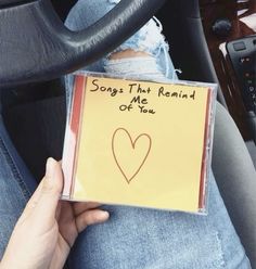 someone is sitting in the car holding up a cd with a heart drawn on it