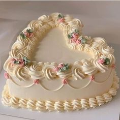 a heart shaped cake with white frosting and pink flowers on it's edges