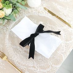 a place setting with white and black napkins, gold utensils and flowers