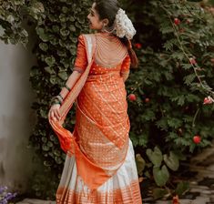 a woman in an orange and white dress standing next to some flowers with her hand on her hip