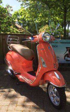 an orange scooter parked in front of a fence