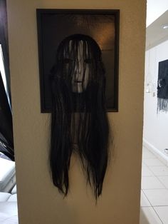 there is a creepy mask hanging on the wall next to a framed photo with long hair