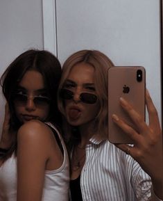 two young women taking a selfie in front of a mirror with their cell phone