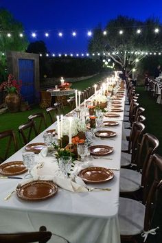 a long table is set with plates and candles for an outdoor dinner party in the evening