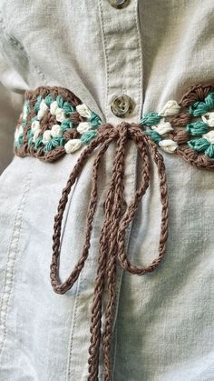 a close up of a person wearing a white shirt with brown and green crochet