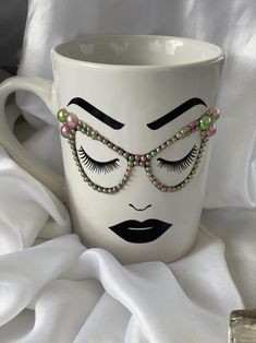 a white coffee cup with a face painted on it and some beads around the eyes