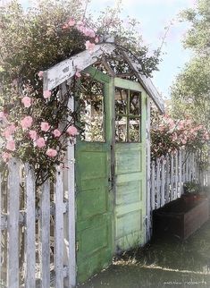 an old outhouse with flowers growing over it's roof and door, next to a white picket fence