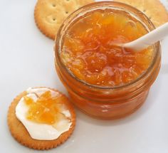 an open jar of jam next to crackers on a white surface with a spoon in it