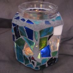 a glass jar filled with lots of different colored tiles on top of a gray surface