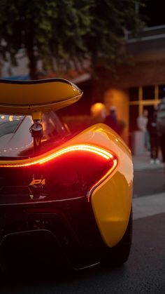 the rear end of a yellow and black sports car with its lights on at night