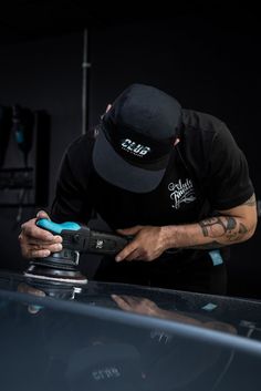 a man in black shirt and hat working on a car with a blue cordless tool