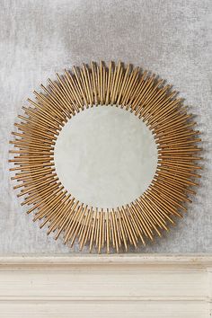 a mirror on the wall above a fireplace mantel with gold sunburst decoration