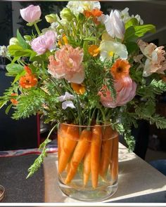 carrots and flowers in a glass vase on a table