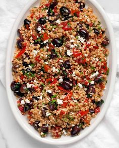 a white bowl filled with rice and black olives on top of a marble table