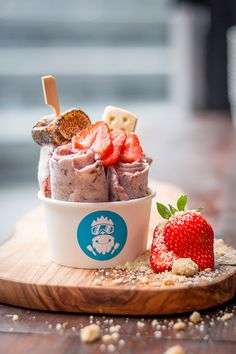 an ice cream sundae with strawberries and crackers on a wooden platter