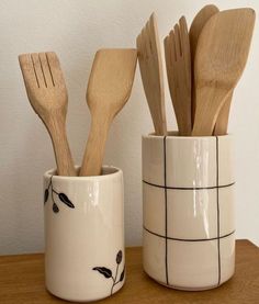 three wooden spoons and two ceramic cups on a table with utensils in them