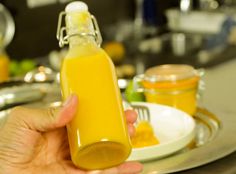 a person holding a bottle of orange juice in front of a plate with food on it