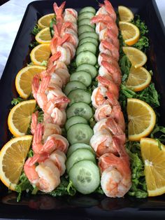 shrimp and cucumbers are arranged on a platter with lemons, cucumbers, and orange slices