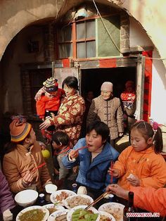 a group of people sitting around a table filled with plates of food and bowls of soup