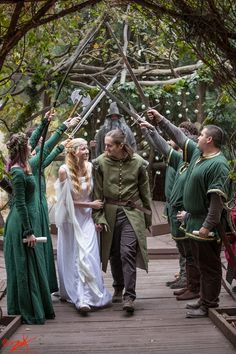 a group of people dressed in medieval clothing walking across a wooden bridge with arms raised