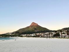 a beach with people walking on the sand and mountains in the backgrouds