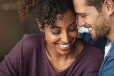 a man and woman smile as they look at each other's cell phone together