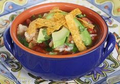 a blue bowl filled with tortilla soup and topped with guacamole