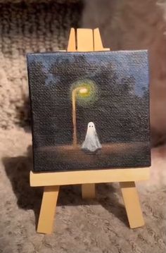 a small easel with a painting on it and a ghost sitting under a lamp