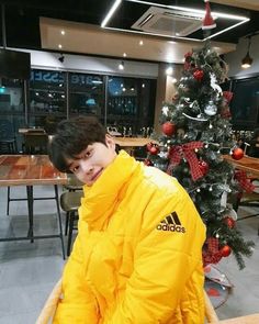 a young man sitting in front of a christmas tree wearing a yellow adidas jacket