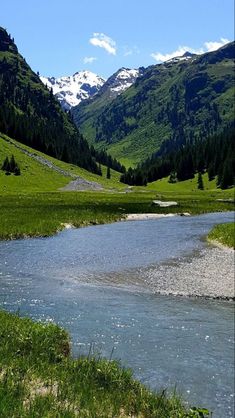 a river running through a lush green hillside covered in snow capped mountains and greenery