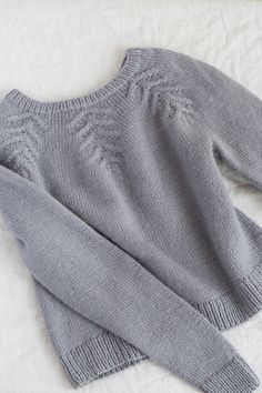 two gray sweaters laying on top of a white blanket