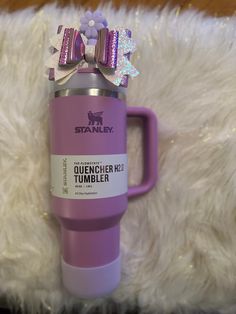 a purple tumbler with a bow on it sitting next to a fluffy white rug