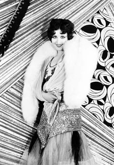 a black and white photo of a woman wearing a fur stole over her shoulders, posing for the camera