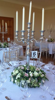 a centerpiece with flowers and candles sits on a table at a formal function in the dining room