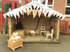 a small wooden structure with some chairs and hay in front of it on the street