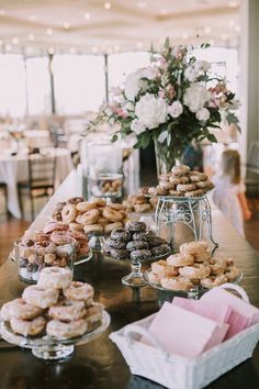 a table filled with lots of donuts on top of glass plates next to flowers