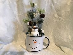 a snowman in a coffee cup with pine cones