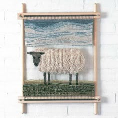 a sheep is standing in front of a wall hanging on a white brick wall,