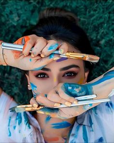 a woman with painted hands holding paintbrushes up to her face