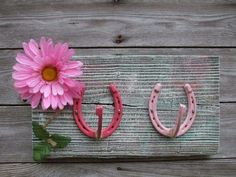 a pink flower sitting on top of a wooden sign with horseshoes attached to it