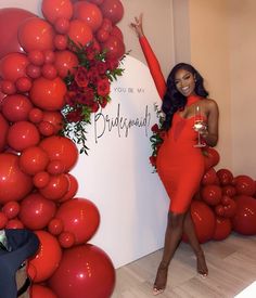 a woman in a red dress standing next to a wall with balloons and flowers on it