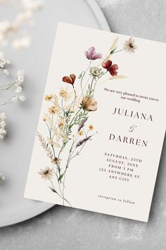 a wedding card with wildflowers on it next to a white plate and flowers