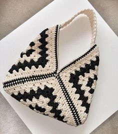 a black and white crocheted purse sitting on top of a white table next to a piece of paper