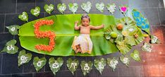 a baby sitting on top of a banana leaf surrounded by flowers and leaves in the shape of numbers